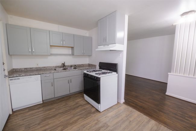 Kitchen featuring wood finished floors, white dishwasher, gas range oven, under cabinet range hood, and a sink | Image 5