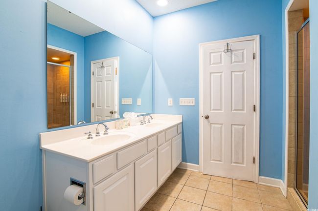 Full bathroom featuring tile patterned floors, a tile shower, double vanity, and baseboards | Image 33