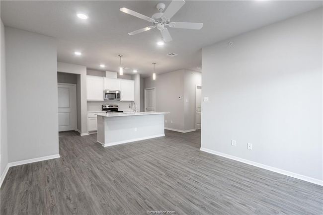 Kitchen featuring stainless steel appliances, white cabinets, hanging light fixtures, dark hardwood / wood-style floors, and a kitchen island with sink | Image 8