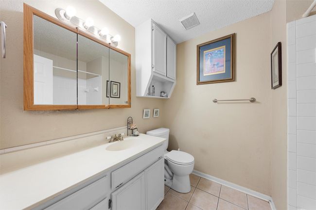 Bathroom featuring toilet, vanity, tile patterned floors, a shower, and a textured ceiling | Image 12