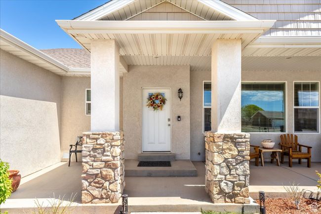 Doorway to property featuring stucco siding, a porch, stone siding, and a shingled roof | Image 4