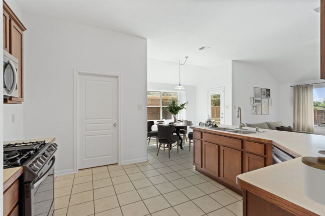 Kitchen with stainless steel appliances, brown cabinetry, light tile patterned floors, lofted ceiling, and decorative light fixtures | Image 13