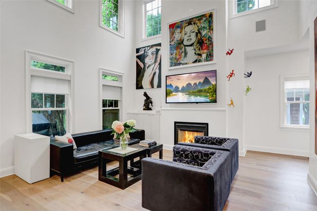 Living room with a high ceiling, light wood-style flooring, a glass covered fireplace, built in shelves | Image 7