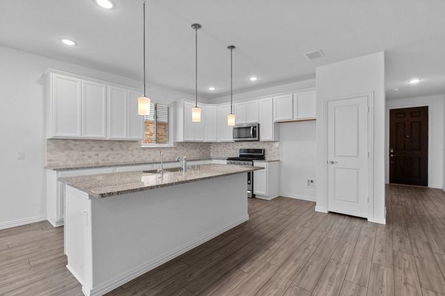Kitchen with stainless steel appliances, white cabinets, a kitchen island with sink, backsplash, and light wood finished floors | Image 6