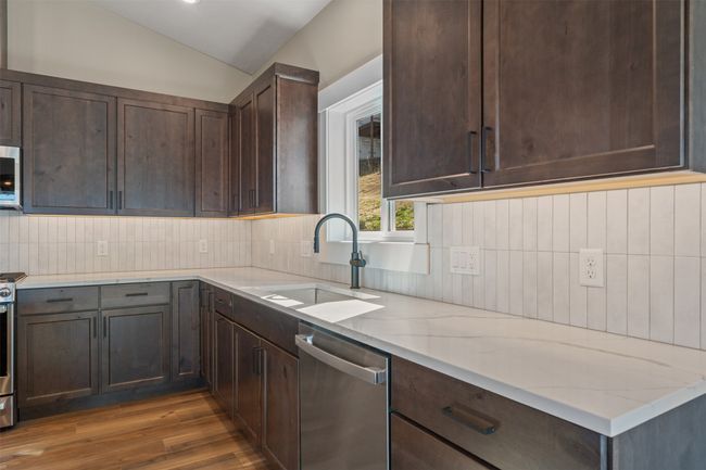 Kitchen with stainless steel dishwasher, a sink, wood finished floors, dark brown cabinetry, and vaulted ceiling | Image 15