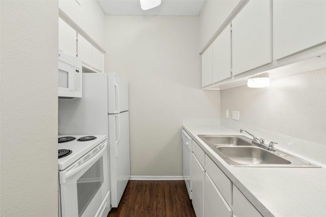 Kitchen with a sink, white appliances, baseboards, light countertops, and dark wood finished floors | Image 11