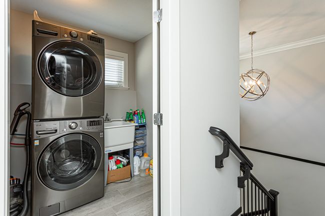 Laundry room featuring crown molding, wood finished floors, stacked washing maching and dryer, an inviting chandelier, and laundry area | Image 15