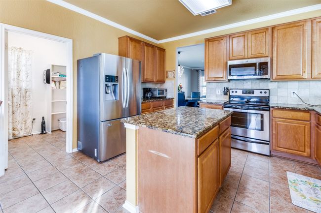 Kitchen with stainless steel appliances, dark stone counters, ornamental molding, a kitchen island, and decorative backsplash | Image 11