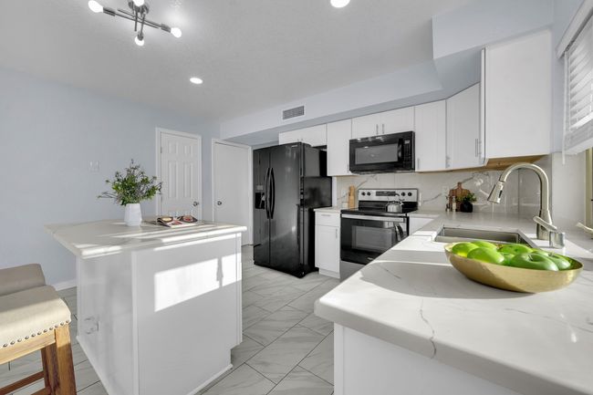 Kitchen featuring black appliances, light marble finish flooring, white cabinets, light stone countertops, and recessed lighting | Image 31