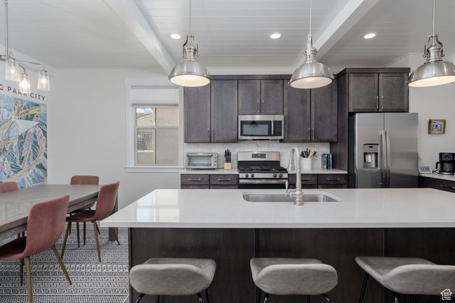 Kitchen featuring stainless steel appliances, a sink, beamed ceiling, a kitchen bar, and light countertops | Image 12