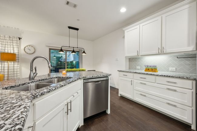 Kitchen featuring white cabinetry, stainless steel dishwasher, a sink, visible vents, and dark wood-type flooring | Image 6
