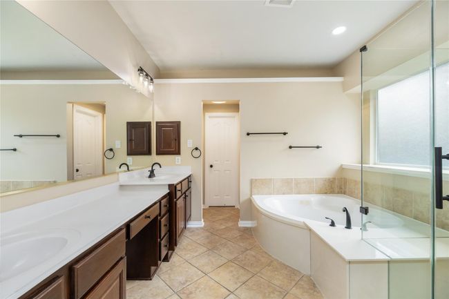This generous bathroom features an expansive vanity with dual sinks, a luxurious soaking tub, and a glass-enclosed shower. | Image 21