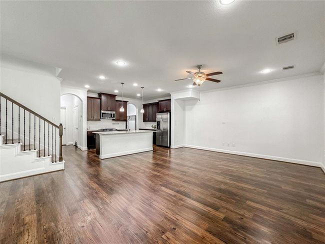 This spacious open-concept room features luxury vinyl floors and a granite kitchen with dark cabinetry, stainless steel appliances, and a central island. Adjacent is a living area with ceiling fan and ample natural light, perfect for entertaining. | Image 4