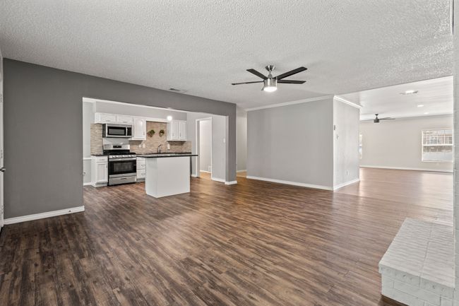 Unfurnished living room with ceiling fan, dark wood-type flooring, baseboards, a textured ceiling, and a sink | Image 9