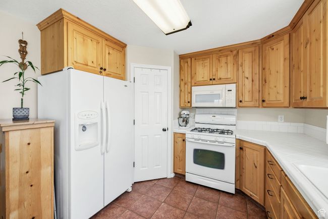 Kitchen featuring white appliances, tile counters, dark tile patterned flooring, and a sink | Image 7