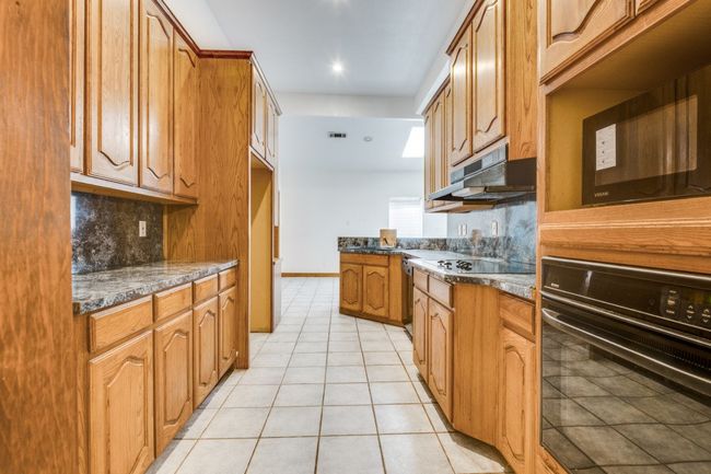 Kitchen with black appliances, under cabinet range hood, light tile patterned floors, decorative backsplash, and brown cabinets | Image 10