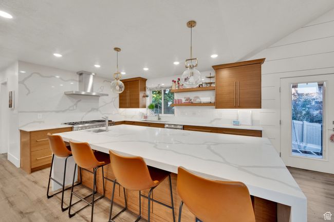 Kitchen with wall chimney exhaust hood, brown cabinets, open shelves, light wood finished floors, and recessed lighting | Image 5