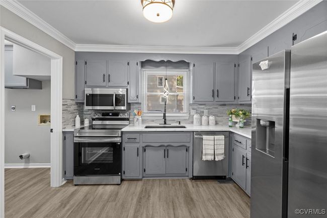 Kitchen featuring gray cabinets, appliances with stainless steel finishes, backsplash, ornamental molding, and light countertops | Image 15