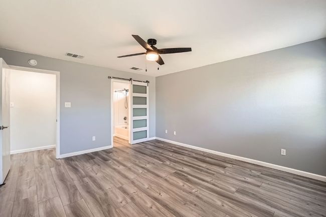 Unfurnished bedroom with wood finished floors, a ceiling fan, visible vents, a barn door, and baseboards | Image 14