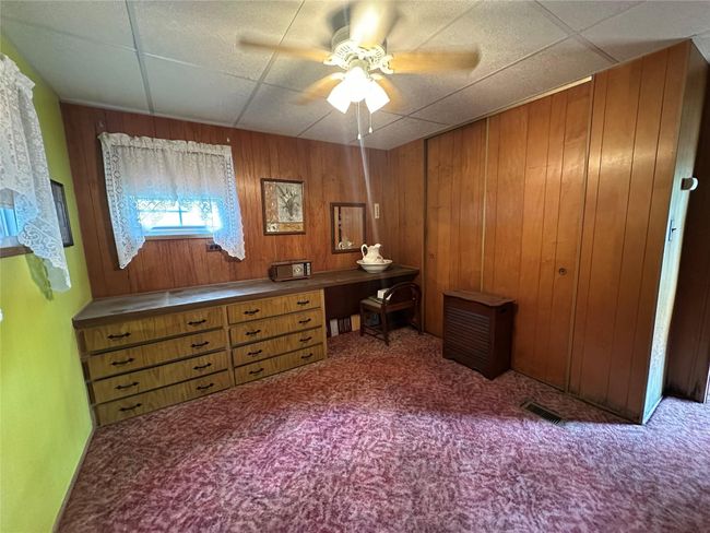 Carpeted bedroom with wood walls, a desk, and a paneled ceiling | Image 13