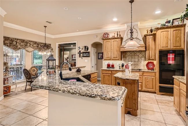 Kitchen with premium range hood, an island with sink, arched walkways, black appliances, and a sink | Image 12