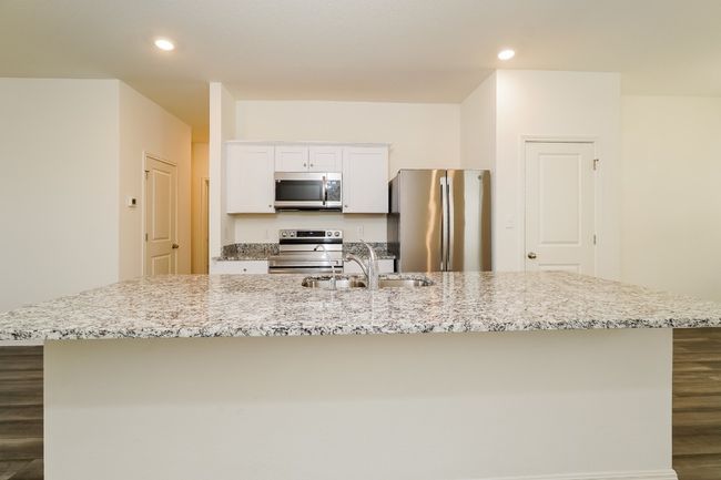 Kitchen with stainless steel appliances, a center island with sink, white cabinetry, dark wood-style floors, and light stone countertops | Image 9