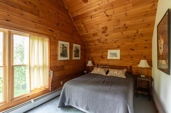 Carpeted bedroom featuring a baseboard heating unit, multiple windows, vaulted ceiling, wooden walls, and wood ceiling | Image 16