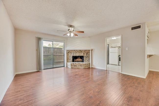 Unfurnished living room featuring ceiling fan, a textured ceiling, wood finished floors, and a fireplace | Image 5