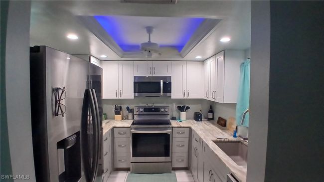Kitchen featuring stainless steel appliances, tray ceiling, sink, and light stone countertops | Image 9