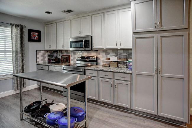 Kitchen featuring stainless steel appliances, decorative backsplash, light vinyl flooring, gray cabinets, and light stone countertops | Image 13