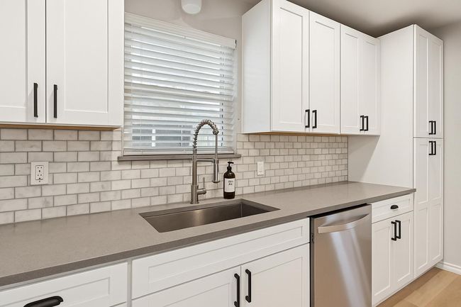 Kitchen featuring stainless steel dishwasher, a sink, white cabinetry, and decorative backsplash | Image 9