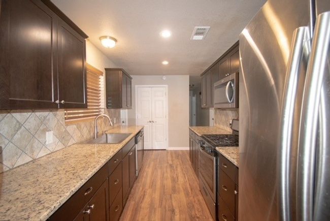 Kitchen featuring appliances with stainless steel finishes, a sink, baseboards, light wood-type flooring, and dark brown cabinets | Image 6