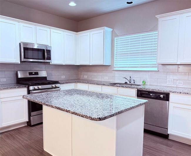 Kitchen with stainless steel appliances, a sink, dark wood-type flooring, a center island, and white cabinets | Image 4