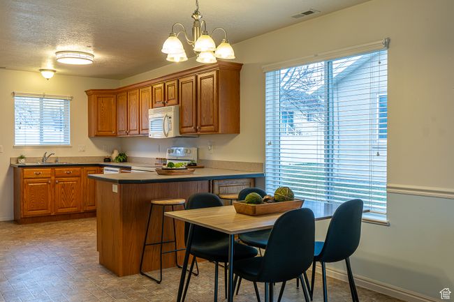 Kitchen with white appliances, visible vents, a peninsula, a notable chandelier, and brown cabinetry | Image 9