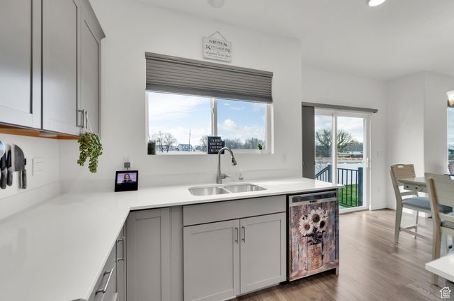 Kitchen featuring light countertops, a sink, wood finished floors, gray cabinetry, and dishwashing machine | Image 8