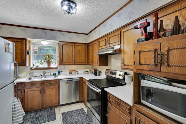 Kitchen with appliances with stainless steel finishes, a sink, a textured ceiling, under cabinet range hood, and light countertops | Image 10