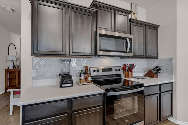 Kitchen featuring stainless steel appliances, decorative backsplash, light wood-type flooring, dark brown cabinetry, and light countertops | Image 13