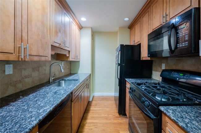 Kitchen featuring dark stone countertops, light wood finished floors, a sink, and black appliances | Image 6