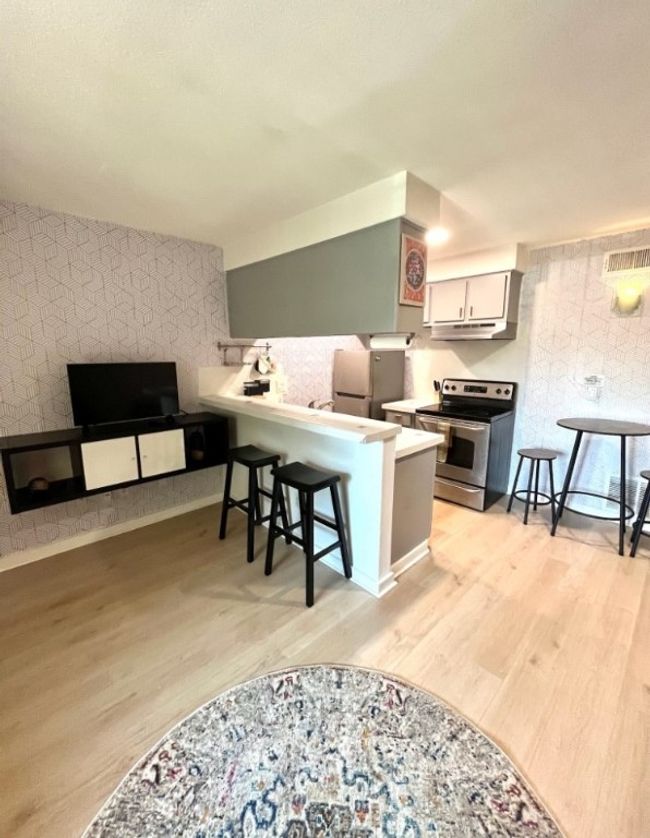 Kitchen with wallpapered walls, a kitchen bar, appliances with stainless steel finishes, light wood finished floors, and a peninsula | Image 4