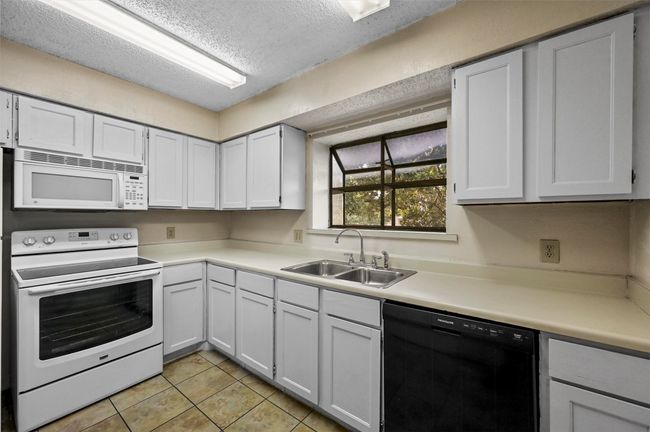 Kitchen featuring white appliances, a textured ceiling, light countertops, light tile patterned flooring, and white cabinetry | Image 8