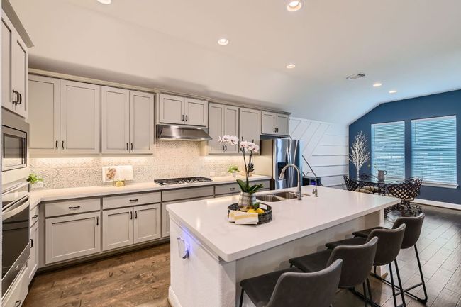Kitchen featuring under cabinet range hood, lofted ceiling, dark wood finished floors, decorative backsplash, and a kitchen breakfast bar | Image 11