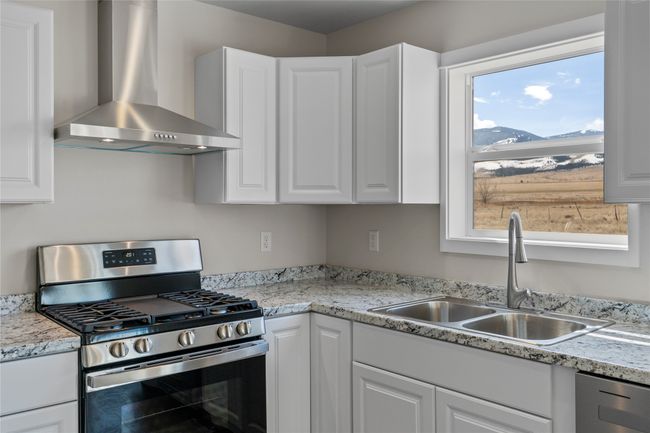 Kitchen with wall chimney range hood, white cabinets, a sink, and stainless steel gas range | Image 37
