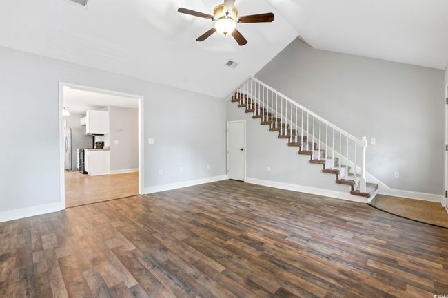 Unfurnished living room featuring a ceiling fan, stairway, dark wood-style flooring, vaulted ceiling, and baseboards | Image 5