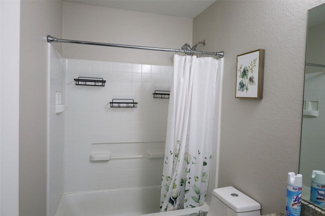 Bathroom with toilet, a textured wall, and shower / tub combo with curtain | Image 9