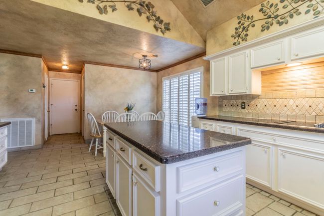 Kitchen featuring tasteful backsplash, white cabinets, crown molding, a kitchen island, and dark stone countertops | Image 7