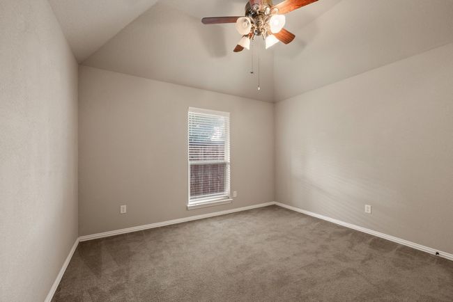 Empty room featuring dark colored carpet, baseboards, vaulted ceiling, and a ceiling fan | Image 26