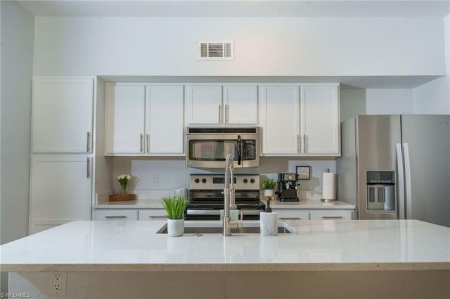 Kitchen with appliances with stainless steel finishes, white cabinets, visible vents, and light stone countertops | Image 7