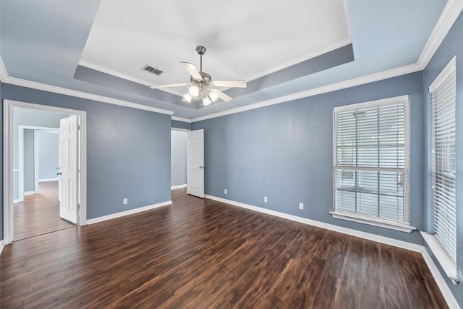 Unfurnished room with a tray ceiling, dark wood-style floors, a ceiling fan, and crown molding | Image 14