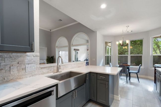 Kitchen with backsplash, dishwasher, a sink, light stone countertops, and a notable chandelier | Image 18