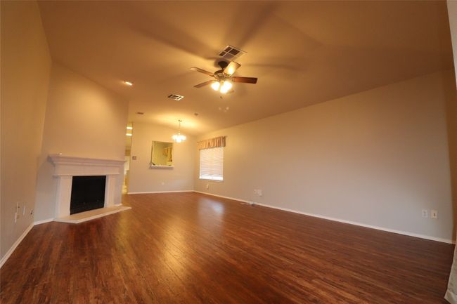 Unfurnished living room featuring lofted ceiling, ceiling fan, dark wood-style flooring, and a fireplace with raised hearth | Image 7
